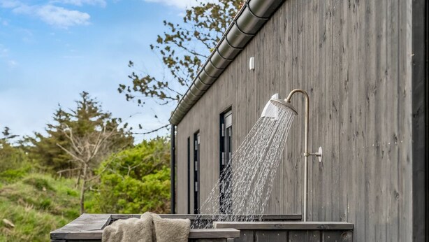 A wooden building with a showerhead mounted on the exterior wall, water flowing from it. - "Uschi" - 1km from the sea by Interhome (Blokhus)