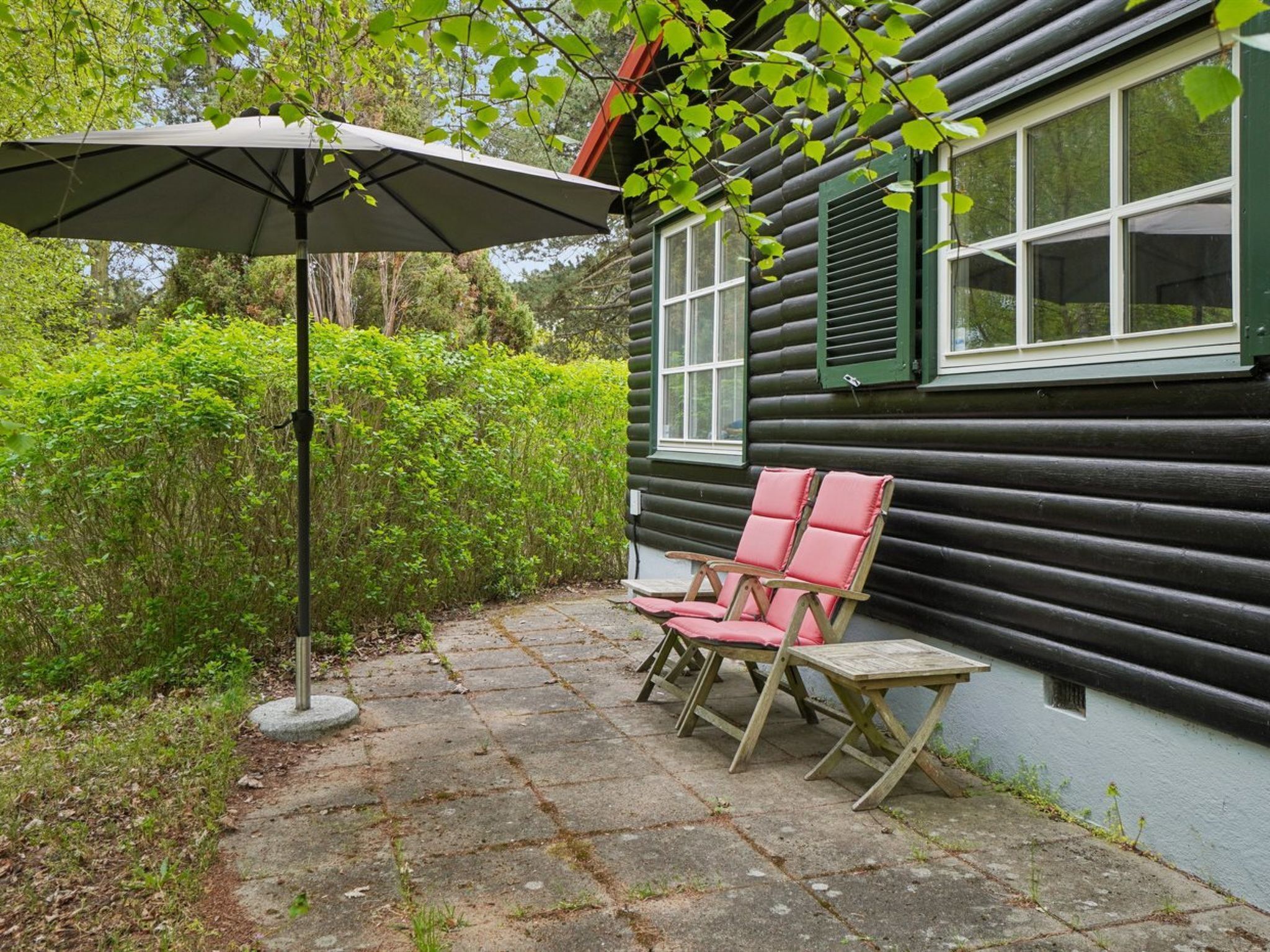 Eine Blockhütte mit einer Terrasse, komplett mit Tisch und Stühlen, einem Sonnenschirm und Blick auf üppiges Grün.