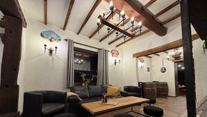Un interior acogedor con techo de madera, sofá de cuero negro, una mesa de madera y taburetes negros.