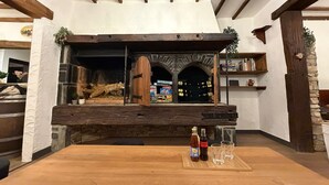 Un interior rústico con chimenea de piedra, vigas de madera y una mesa con botellas y vasos.