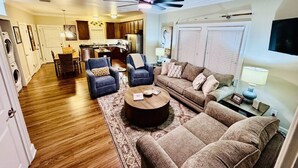 A spacious living room with a large sofa, two armchairs, a coffee table, and a dining area with a table and chairs.
