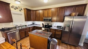 A kitchen with wooden cabinets, stainless steel appliances, a granite countertop island, and a trash can.