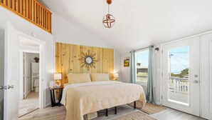 A bedroom with a wooden headboard, a large bed, a hanging light fixture, and a view through a door. - #StayInMyDistrict Strandhuisje Oceanview Retreat (Rockaway Beach)