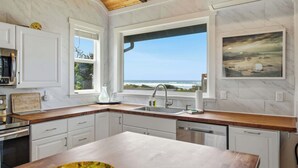 A kitchen with a view of the ocean, white cabinets, and a wooden ceiling. - #StayInMyDistrict Strandhuisje Oceanview Retreat (Rockaway Beach)