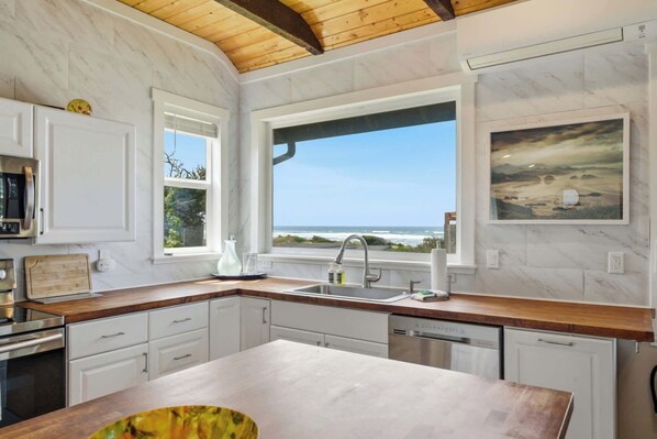 A kitchen with a view of the ocean, white cabinets, and a wooden ceiling.