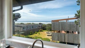 A view from a window overlooking a wooden deck, a grassy yard, and a beach with the ocean in the background. - #StayInMyDistrict Strandhuisje Oceanview Retreat (Rockaway Beach)