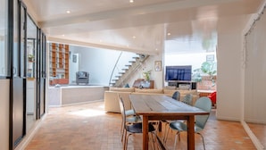 Amplia sala de estar con una mesa de comedor, sillas, un sofá y una escalera que conduce a un nivel superior.