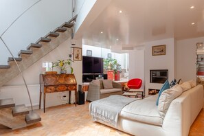 Un salon moderne avec un escalier, un canapé, un téléviseur et un coin repas.