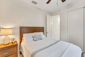 Ein ordentlich bezogenes Bett mit weißen Leinen und einem Holz-Kopfteil, ein Nachttisch mit Lampe und eine Tür zur rechten Seite.
