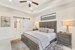 Une chambre à coucher avec un lit, des tables de chevet, un ventilateur de plafond et une fenêtre.