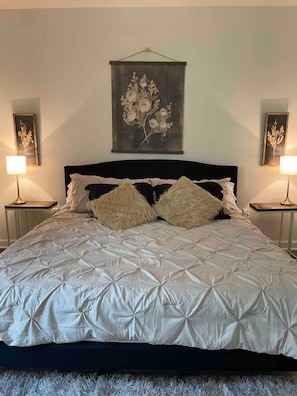 Una cama con cubrecama acolchado, dos lámparas de noche y una obra de arte floral en la pared.