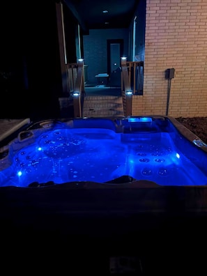 Un jacuzzi con iluminación azul, un muro de ladrillo y una escalera que conduce a un nivel superior.
