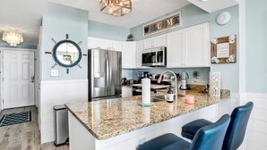 Una cocina moderna con armarios blancos, encimera de granito y una isla central con taburetes de bar.