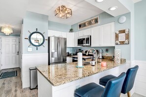 A modern kitchen with white cabinetry, a granite countertop, and a central island with bar stools.