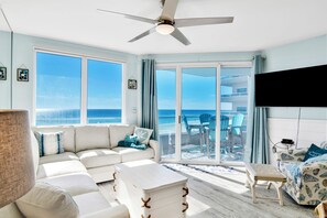 A spacious living room with a large window, a ceiling fan, and a view of the ocean.