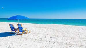 Una playa con dos sillas azules y una sombrilla azul bajo un cielo despejado.