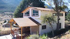 Une maison à deux étages dotée d’un porche couvert, d’une antenne parabolique et offrant une vue sur une vallée.