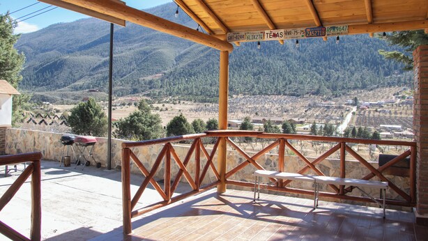 Une terrasse couverte offrant une vue sur un paysage montagneux, avec une balustrade en bois et une table.