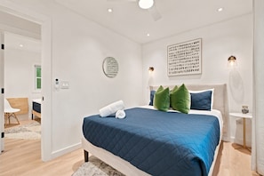 Ein modernes Schlafzimmer mit einem großen Bett, einem Wandbild, einem Deckenventilator und einem Nachttisch mit einer Lampe.