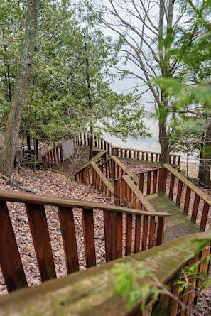 Un escalier en bois mène à une zone de plage entourée d’arbres.