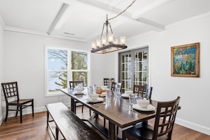 Une salle à manger avec une table en bois, des chaises, un banc, un lustre et un tableau accroché au mur.