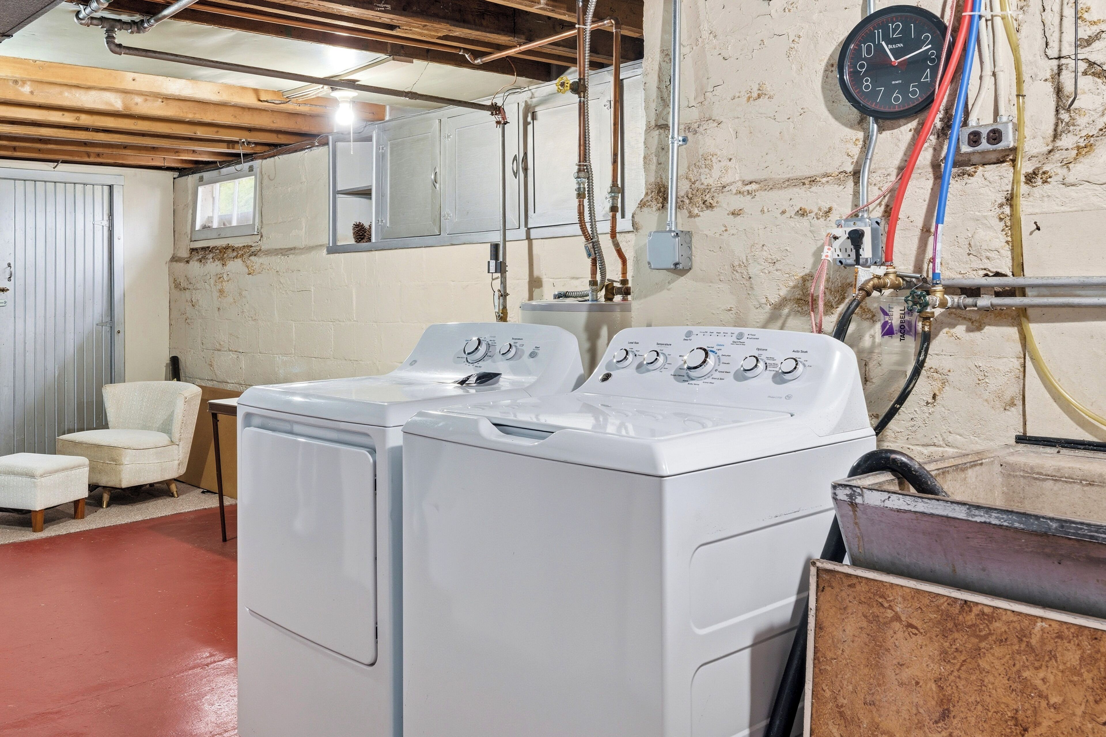 A laundry room with a front-loading washer and dryer, a clock, and visible plumbing.