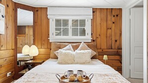 Un dormitorio con pared de paneles de madera, una cama grande con almohadas mullidas, una mesita de noche con una lámpara y una bandeja con muffins y tazas de café.