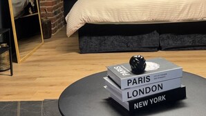 A loft-style bedroom with a sloped ceiling, a skylight, a bed, a small table with books, and a brick wall. - Maison Soleya -Wellness escape with spa & jacuzzi (Asse)
