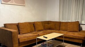 A living room with a brown sectional sofa, a wooden coffee table, and a white wall with abstract art. - Maison Soleya -Wellness escape with spa & jacuzzi (Asse)