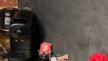 Una cuina amb un taulell, una cafetera, un recipient de vidre, un safata i un ram de roses vermelles.