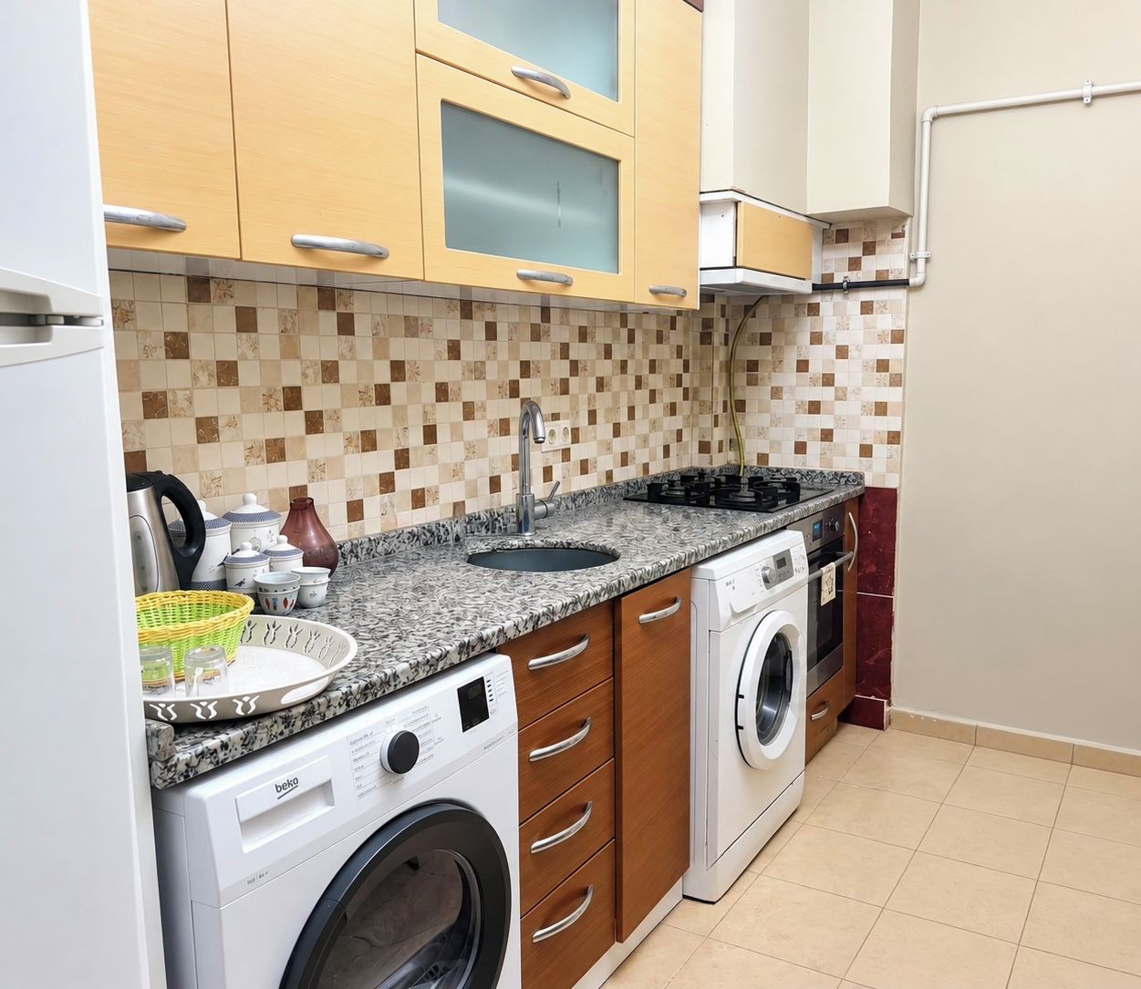 Une cuisine de taille réduite, équipée d’un lave-linge, d’un évier et de meubles de rangement en bois.