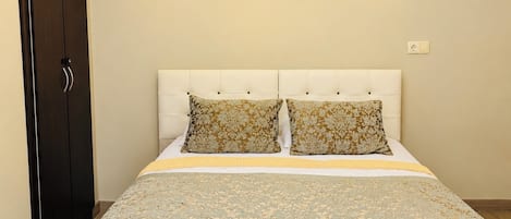 A bedroom with a bed, two pillows, a headboard, a painting on the wall, and a wardrobe.