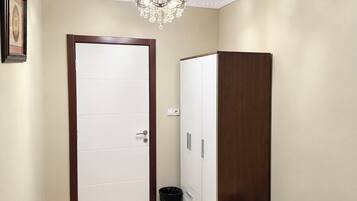 A hallway with a white door, a wooden wardrobe, a trash bin, and a chandelier.