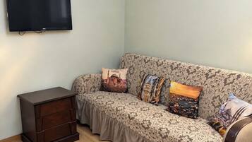 A living room with a sofa, a TV mounted on the wall, and a small wooden cabinet.