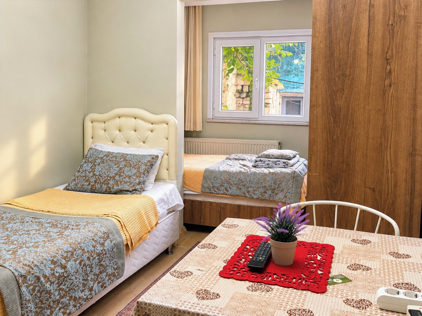 Een slaapkamer met twee bedden, een raam met uitzicht, een tafel met een afstandsbediening en een plant, en een witte stoel.