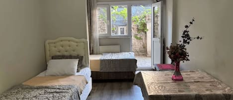 A bedroom with two beds, a table with a vase, and a view of the outside.