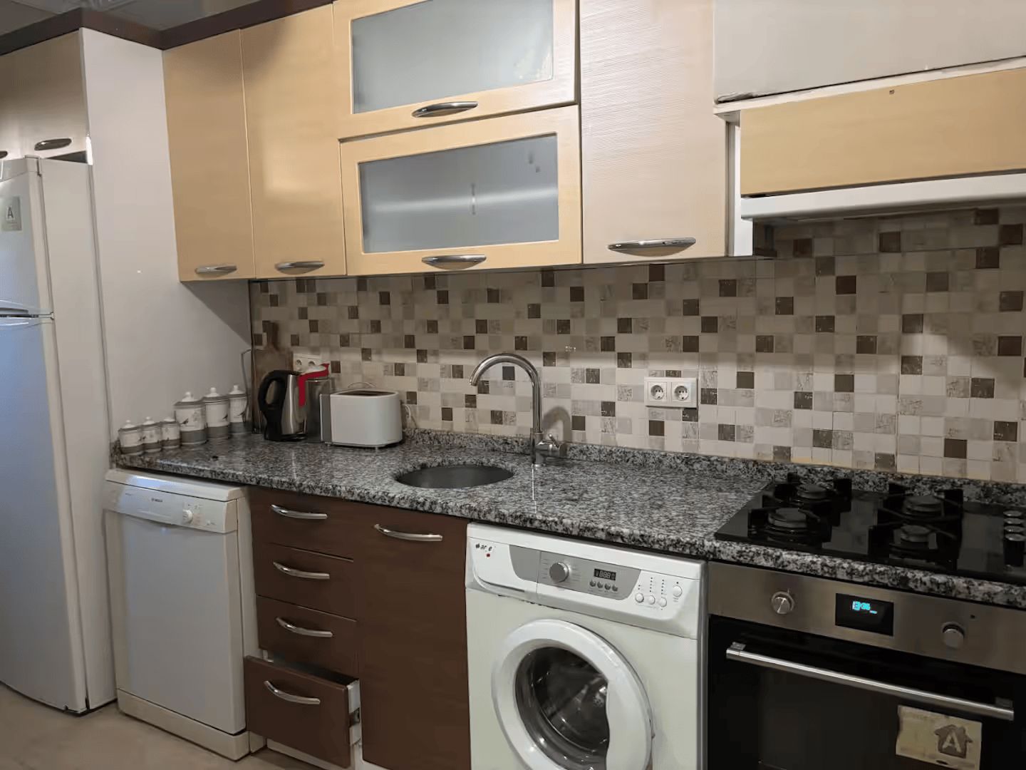 A compact kitchen with a dishwasher, washing machine, and a stove.