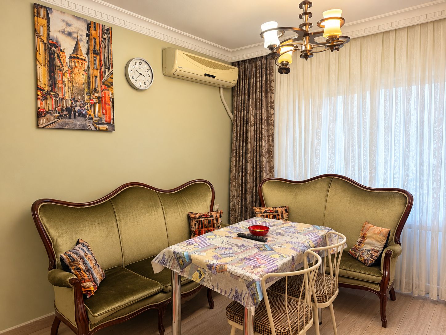 A dining area with a table set for four, flanked by two green upholstered sofas with patterned cushions.
