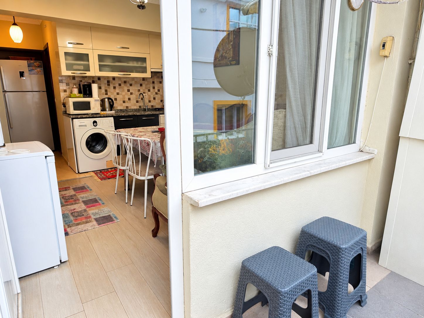 Een praktische keuken met een wasmachine, een eethoek met een tafel en stoelen, en een raam met uitzicht op het omliggende landschap.