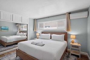 Ein Hotelzimmer mit zwei Betten, einem Fenster mit Vorhängen, einem Nachttisch mit Lampe und einer Wand-Klimaanlage.