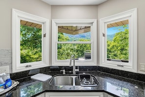 A kitchen with a sink, a window with a view of greenery, and a countertop with a dish rack. - Greystone Retreat at Lake Lure - Rumbling Bald Resort - 3BR, 2.5BA - As seen on HGTV - Great Views (Lake Lure)