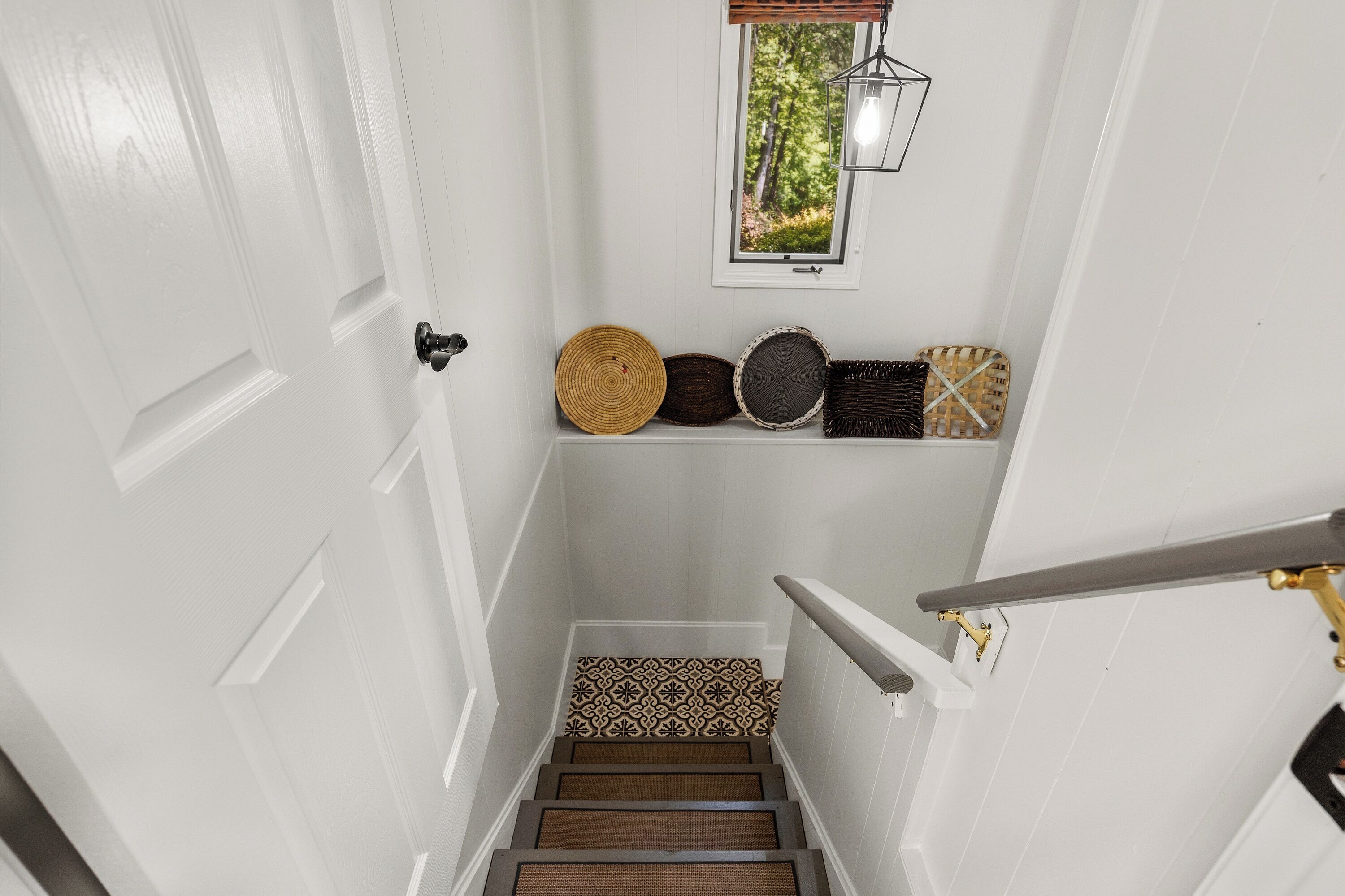 A staircase with a patterned carpet, a wall-mounted light fixture, and a window with a view of trees.