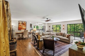 A spacious living area with a sofa, dining table, and chairs, a ceiling fan, and large windows offering a view of the outdoors. - Greystone Retreat at Lake Lure - Rumbling Bald Resort - 3BR, 2.5BA - As seen on HGTV - Great Views (Lake Lure)