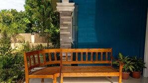 Un banco de madera con respaldo y asiento, ubicado en un patio con suelo de baldosas.