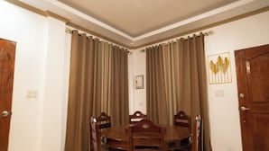 Un comedor con una mesa redonda y sillas, cortinas marrones y un cuadro en la pared.