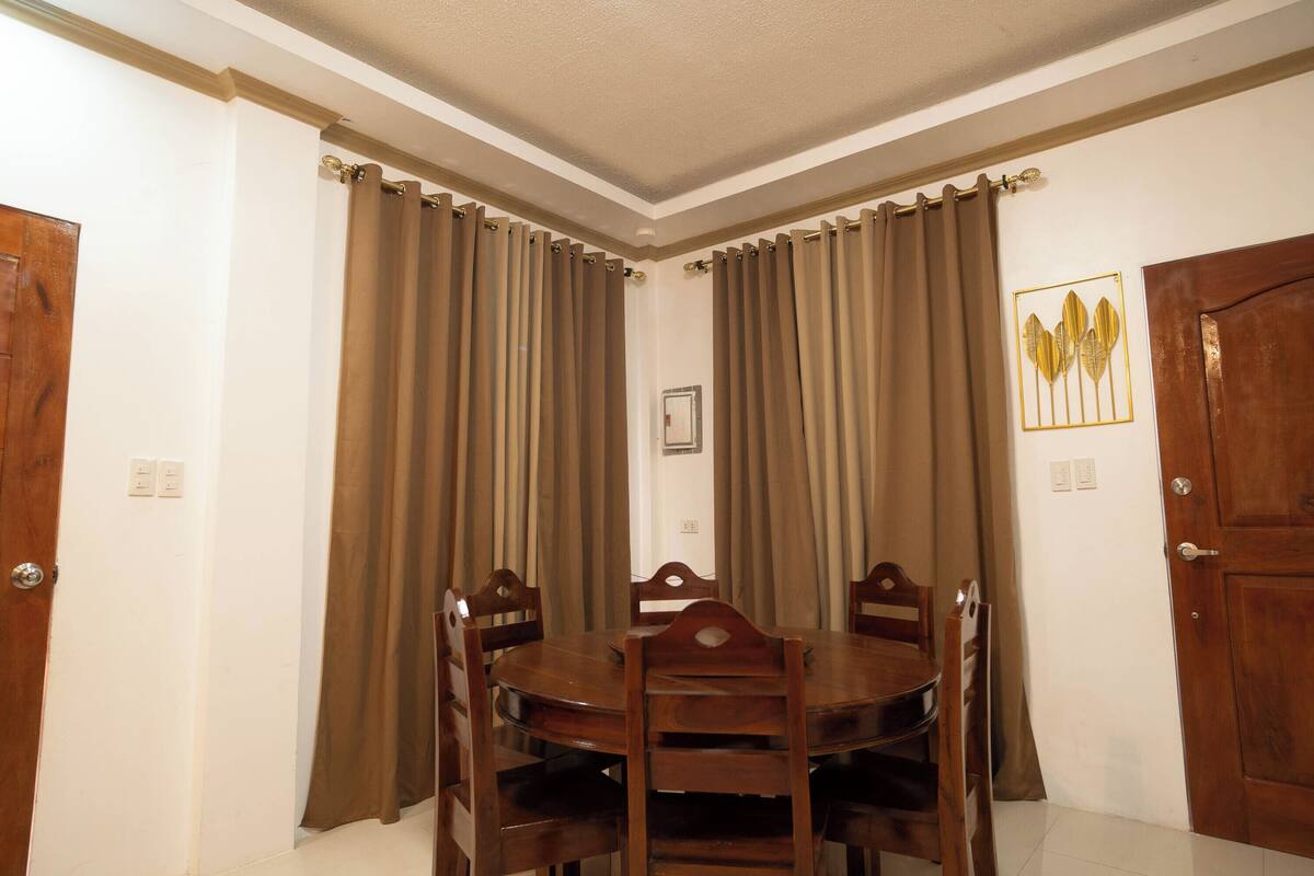 A dining area with a round table and chairs, brown curtains, and a framed picture on the wall.