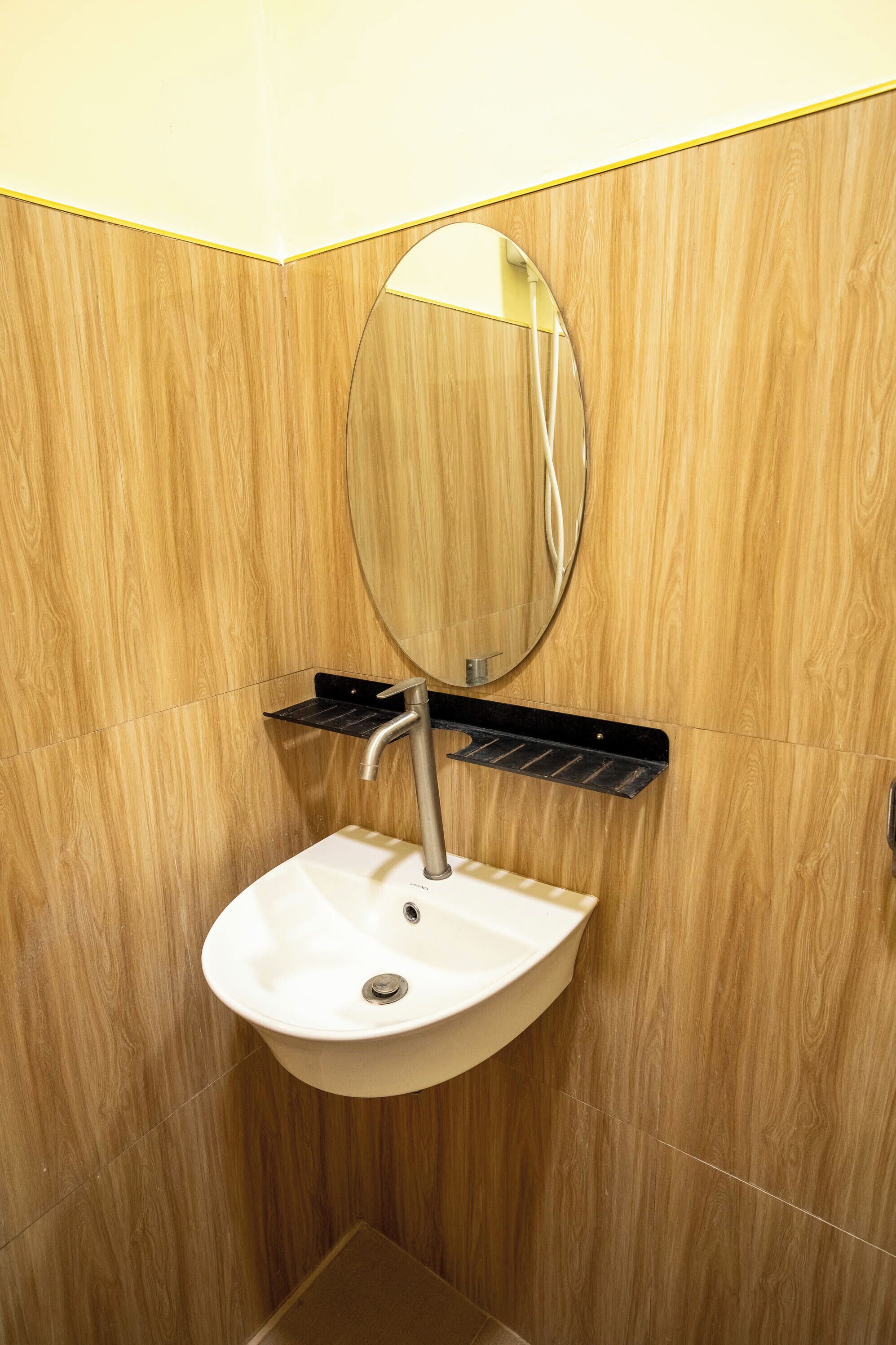 A bathroom with a wooden wall, a white sink, a mirror, and a black towel rack.