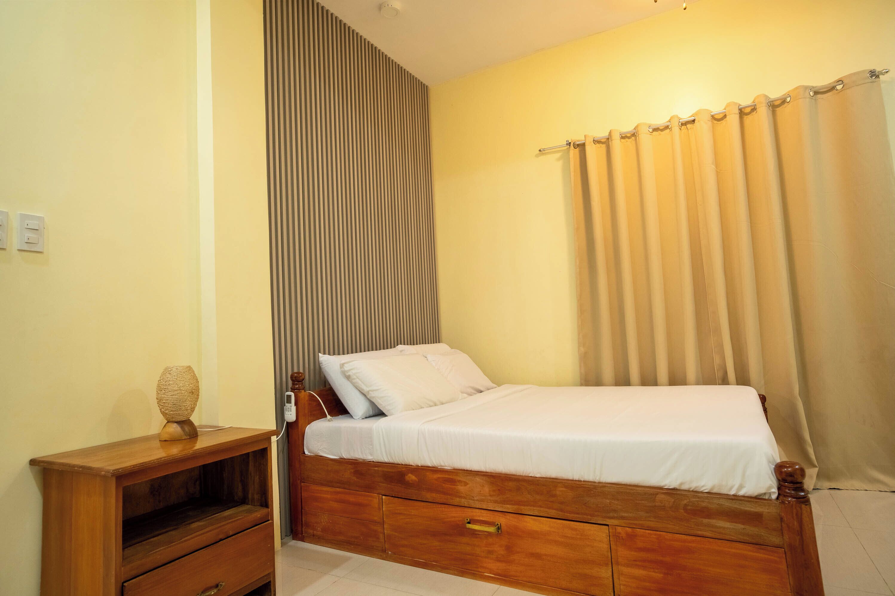 A single bed with a wooden frame, a bedside table, and a wall-mounted light fixture.
