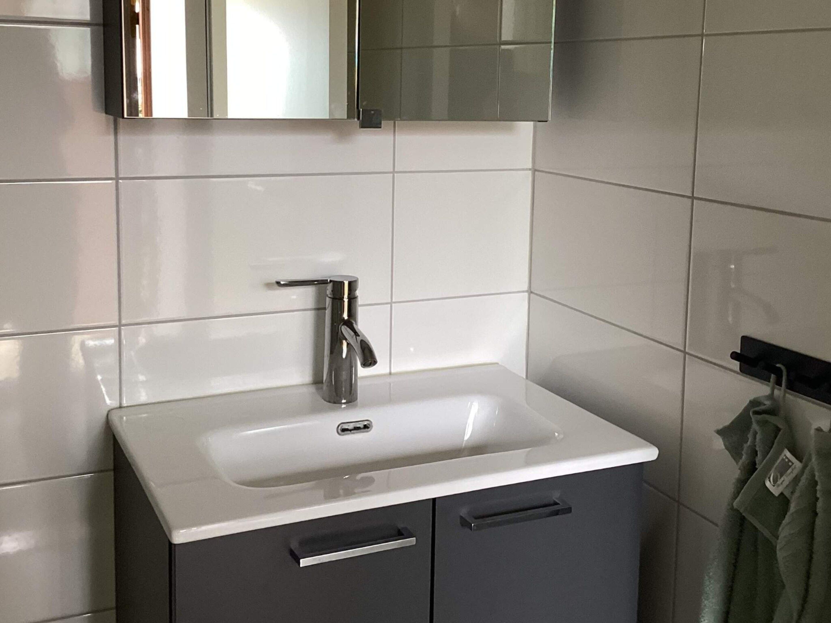 A bathroom with a white sink, a mirror above it, and a towel rack to the right.