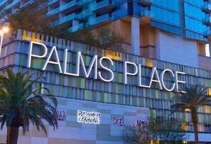 Ein Gebäude mit der Beschilderung 'PALMS PLACE', einem sichtbaren Schild für 'BODYHEAT TANNING' und Palmen davor.